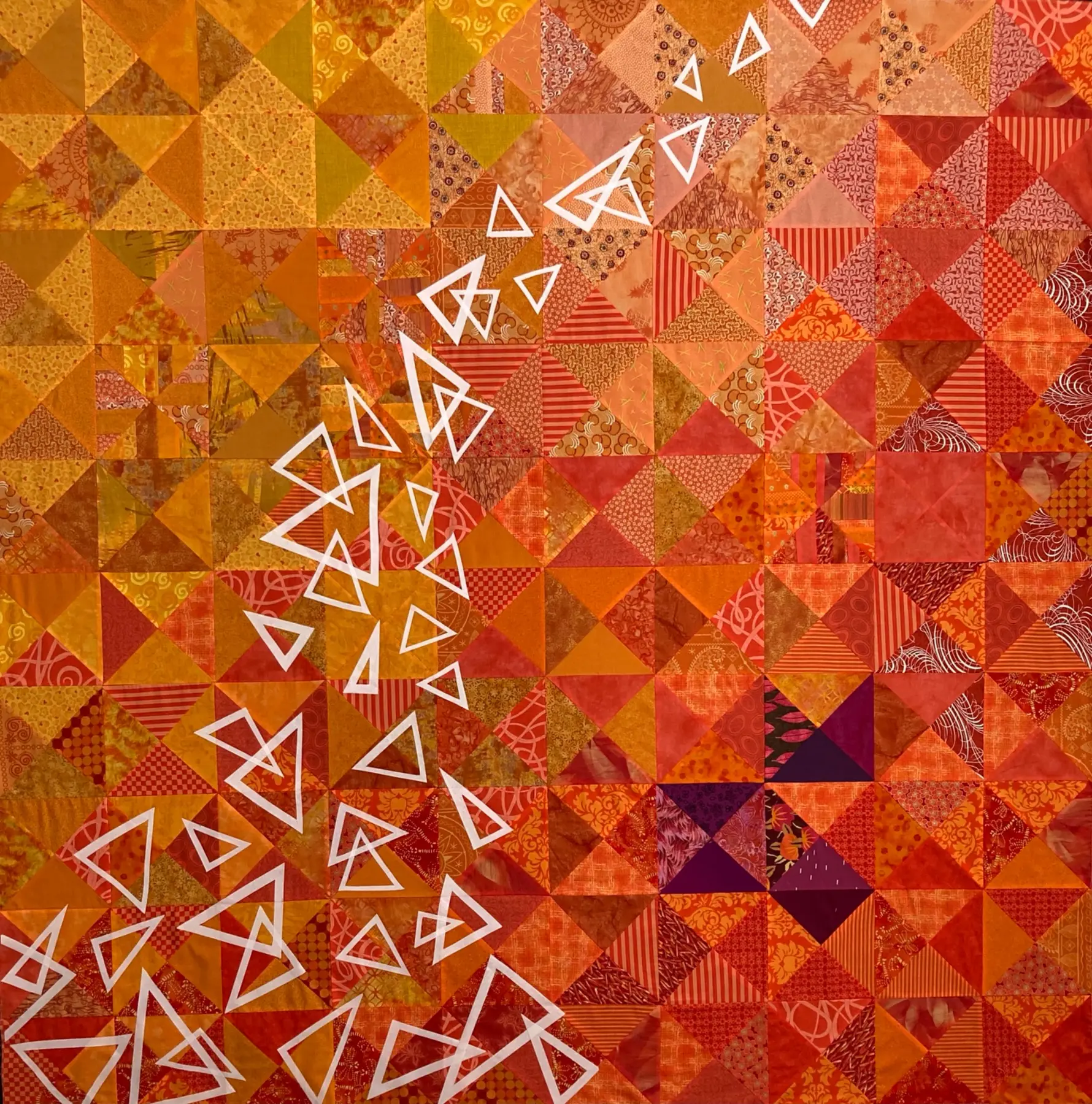 Orange geometric art quilt with white fractured triangular forms moving diagonally across it
