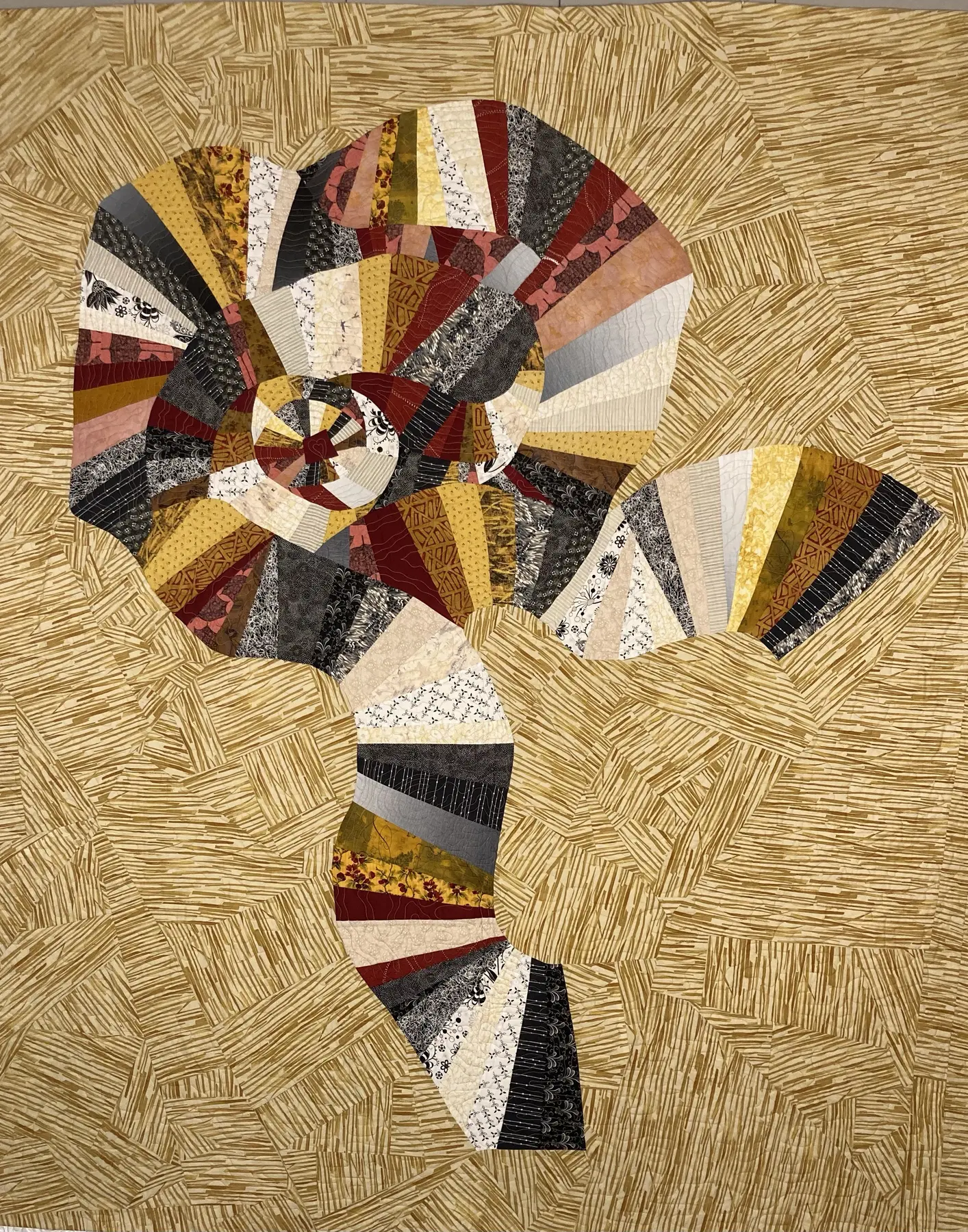 Art quilt with a curving ribbon-like form made of muted patterned fragments on a pale ground