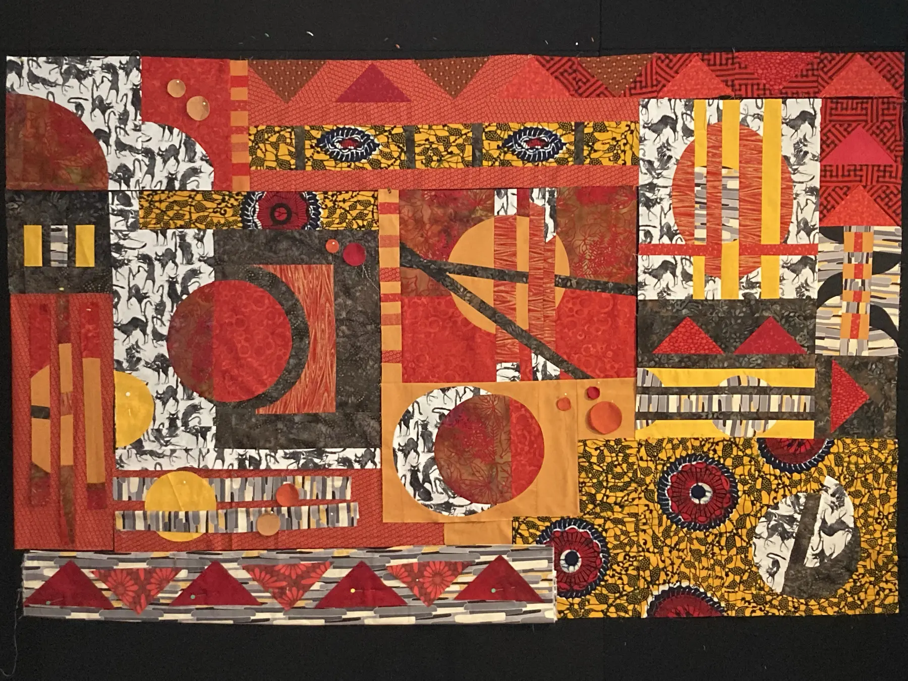 Art quilt with overlapping red, orange and black circular forms and patterned fragments